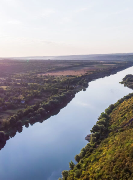 River flowing between a hill with slope covered with greenery and village on the other side, view from the drone in Moldova